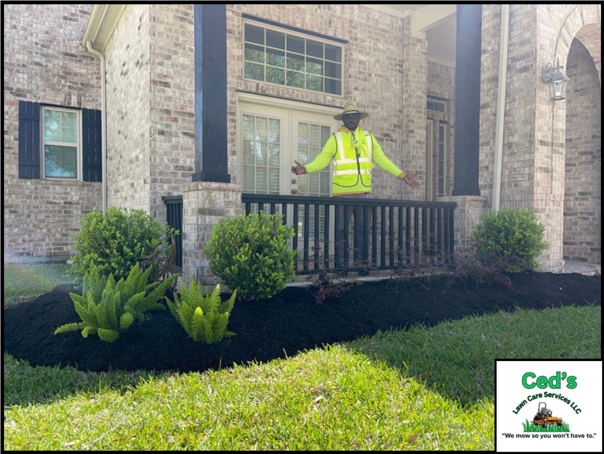 Fresh mulch and trimmed plants near a brick porch with the owner standing behind the rail