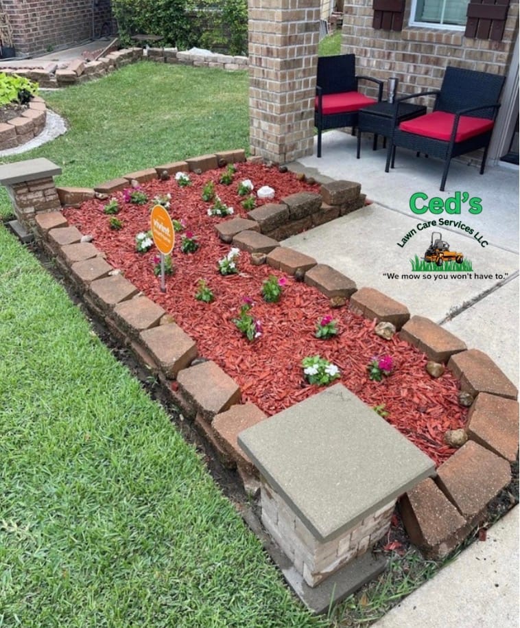 Red mulch flower bed with border stones and small flowers beside a patio